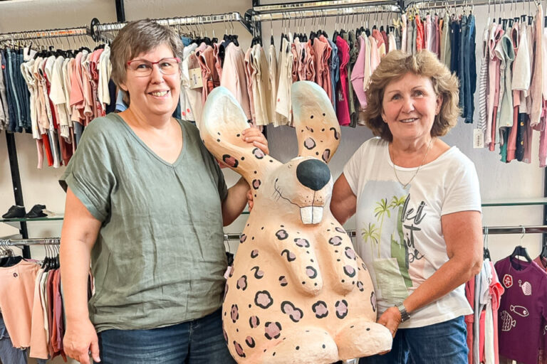 Zwei Frauen stehen lächelnd in einem Kleiderladen und halten gemeinsam eine grosse Plüschfigur eines Hasen.