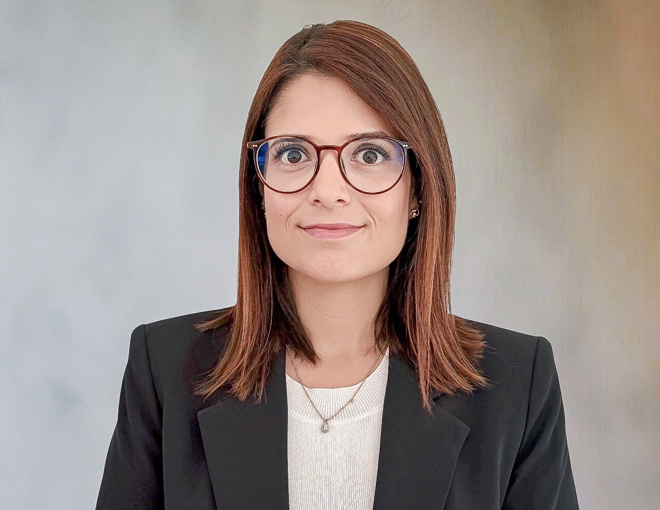 Frau mit schulterlangem braunem Haar und Brille im dunklen Blazer blickt in die Kamera.
