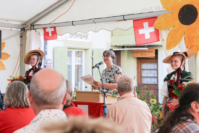 Eine Frau hält am Rednerpult eine Rede, daneben zwei Frauen in Trachten, davor sitzt das Publikum in einem Festzelt.