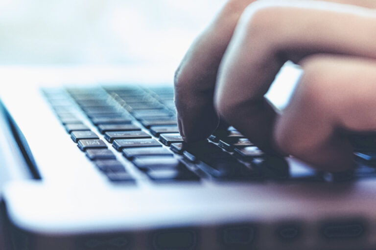 Eine Hand tippt auf der Tastatur eines Laptops, Nahaufnahme mit unscharfem Hintergrund.