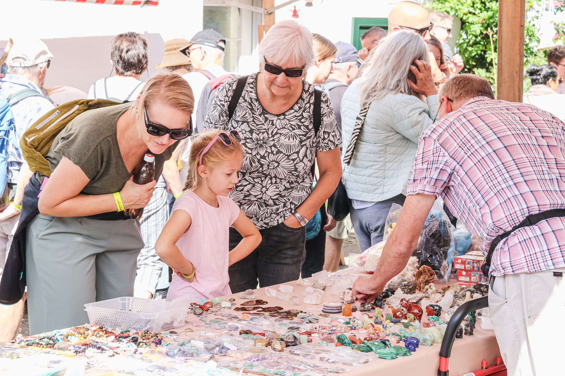 Eine Frau, ein Mädchen und eine ältere Frau betrachten Schmuck und Steine an einem Marktstand.