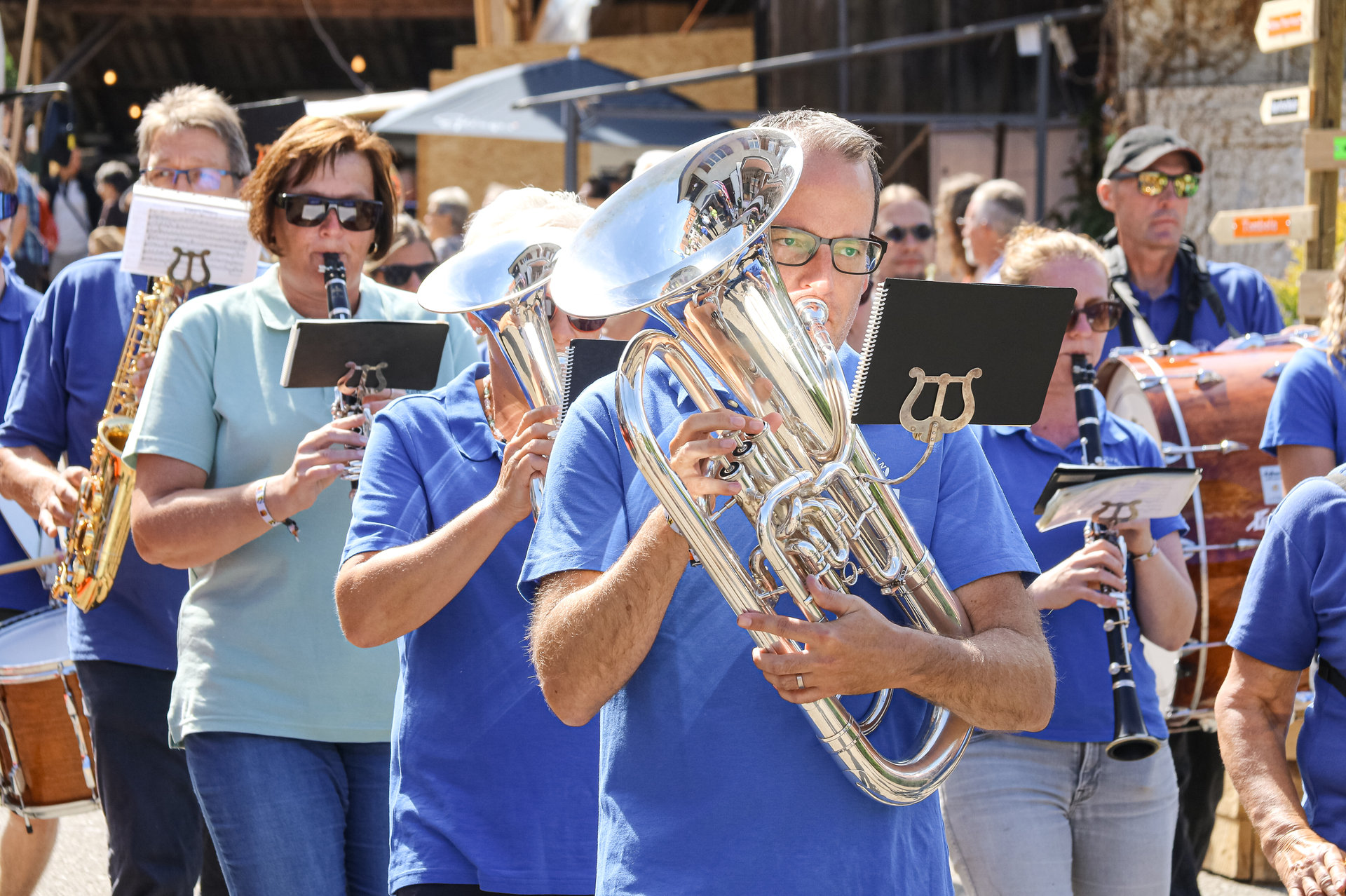 Musikkapelle in blauen Shirts spielt im Freien Blasinstrumente, im Vordergrund ein Mann mit Tenorhorn.