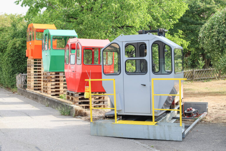 Mehrere bunte Seilbahn- oder Standseilbahnkabinen ohne Fahrgestell stehen aufgereiht am Strassenrand.