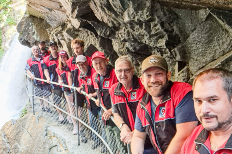 Eine Gruppe von Menschen in roten Westen steht entlang eines schmalen Felsenpfads neben einem Wasserfall.