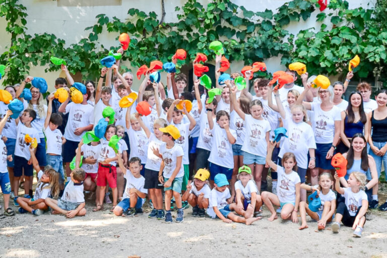 Grosse Gruppe von Kindern und Betreuenden posiert vor einem Haus, viele strecken bunte Wasserpistolen in die Luft.