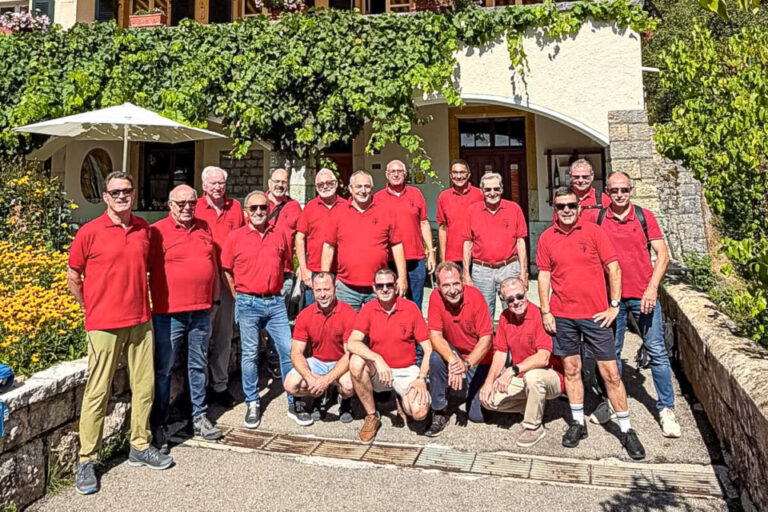 Gruppe Männer in roten Poloshirts posiert vor einem Riegelhaus mit Rebstöcken an der Fassade.