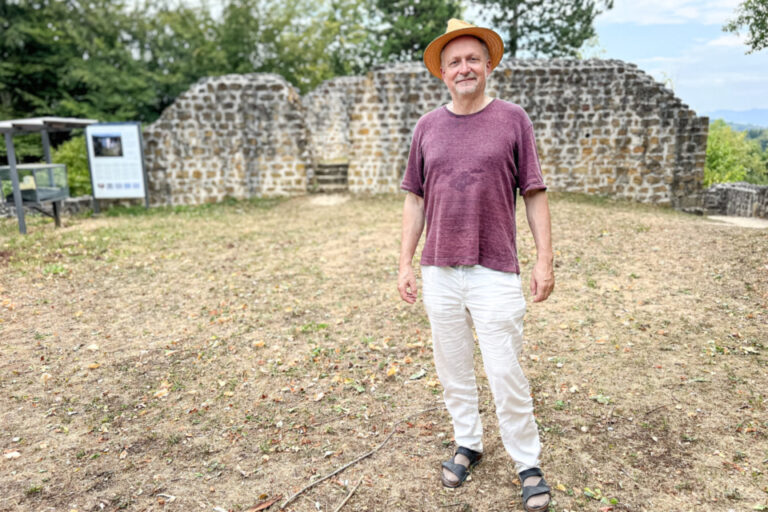 Ein Mann mit Strohhut und rotem T-Shirt steht vor einer alten Steinmauerruine.
