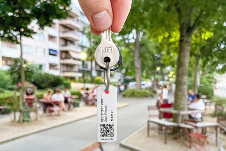 Eine Hand hält einen Schlüssel mit einem Anhänger mit QR-Code in die Luft, im Hintergrund ein Park.