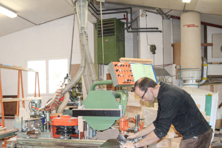 Ein Mann mit Brille bedient eine grosse Holzbearbeitungsmaschine in einer Werkstatt.