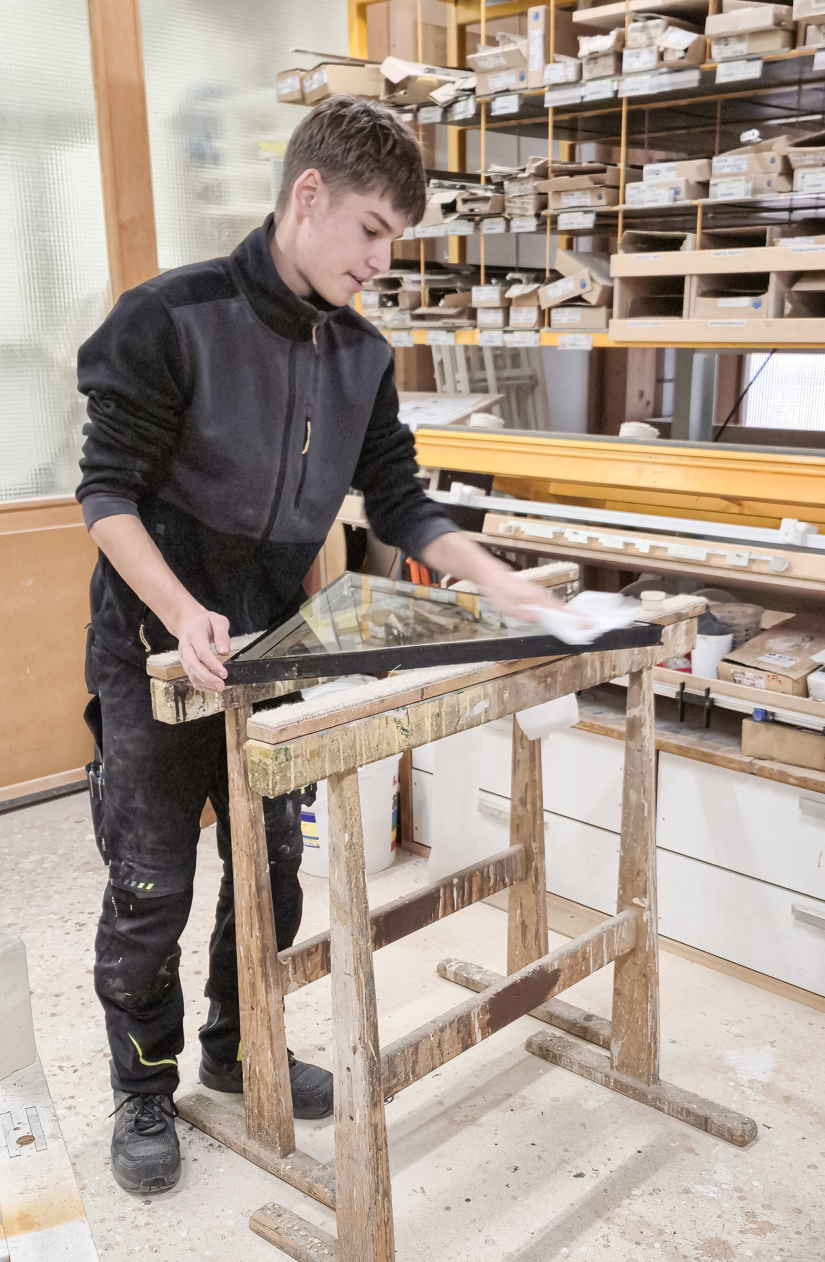 Ein junger Mann in Arbeitskleidung bearbeitet ein Werkstück auf einem Holzbock in einer Werkstatt.