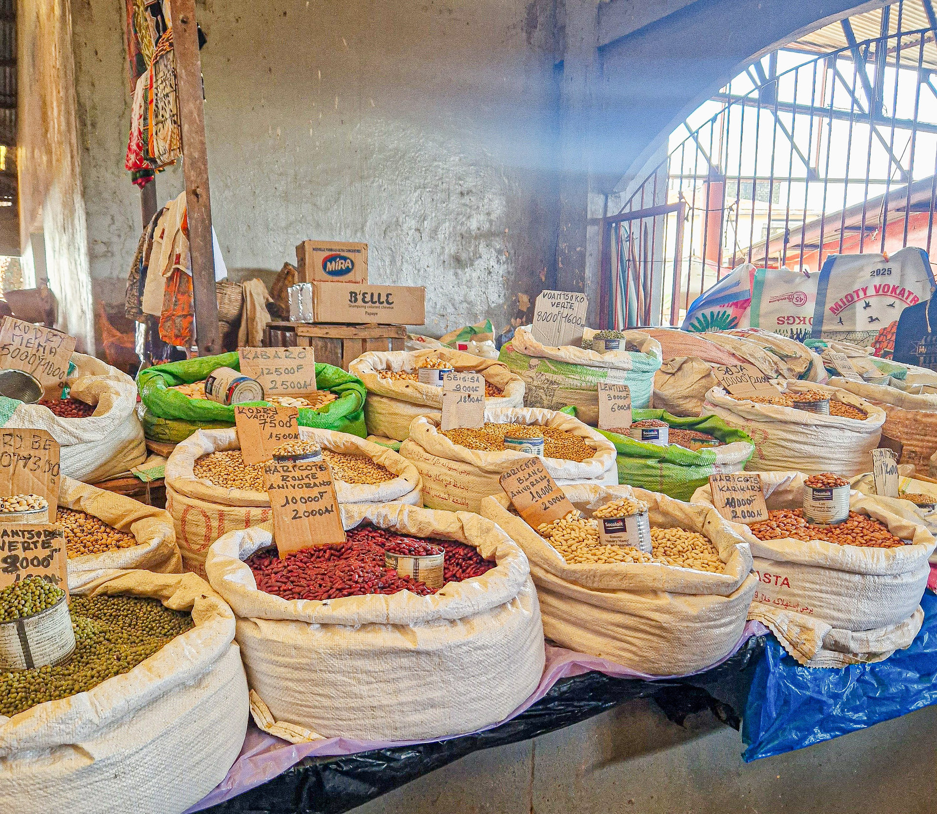 Grosse Säcke mit verschiedenen Bohnen, Erdnüssen und Hülsenfrüchten stehen mit Preisschildern nebeneinander in einer Markthalle.