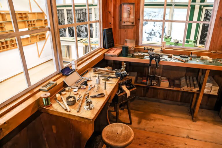 Historische Werkbank mit Uhrmacherwerkzeugen vor einem Fenster in einer Holzwerkstatt.