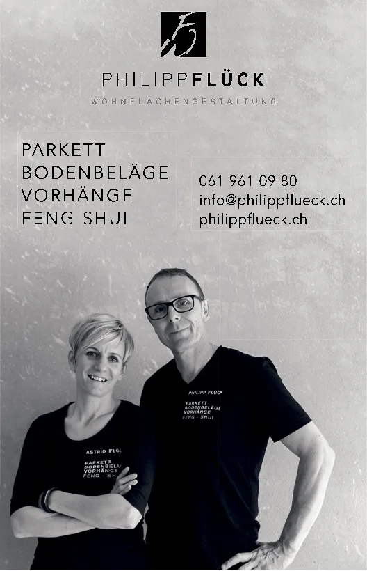 Ein Mann und eine Frau in schwarzen T-Shirts posieren nebeneinander vor einer grauen Wand.