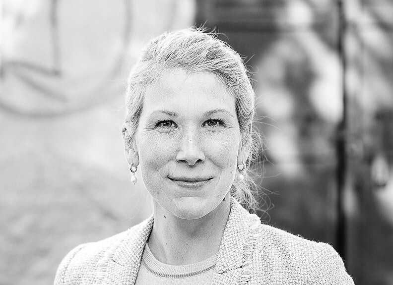 Schwarz-weißes Porträt einer lächelnden Frau mittleren Alters mit hochgestecktem Haar, im Freien.