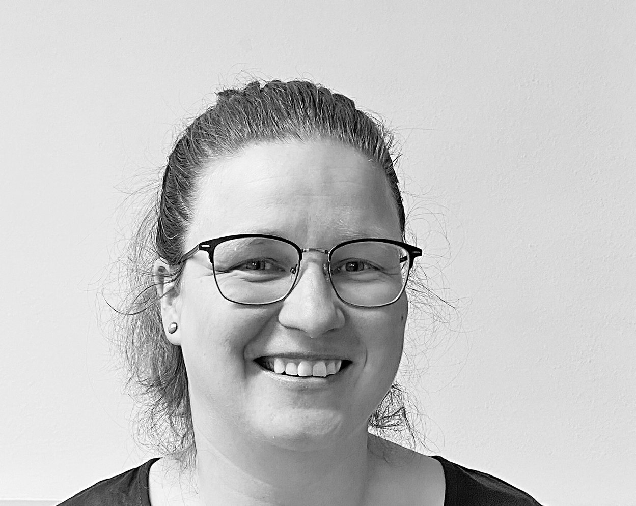 Eine lächelnde Frau mittleren Alters mit Brille und zurückgebundenem Haar in Schwarz-Weiß.