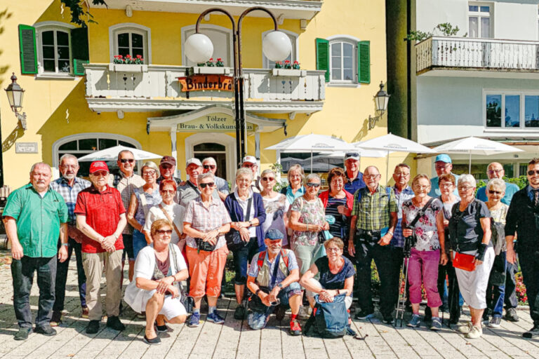 Eine grosse Gruppe von Menschen steht und kniet für ein Gruppenfoto auf einem gepflasterten Platz vor historischen Gebäuden.