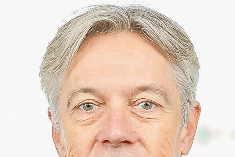 Ein grauhaariger Mann mittleren Alters im dunklen Sakko blickt lächelnd in die Kamera.
