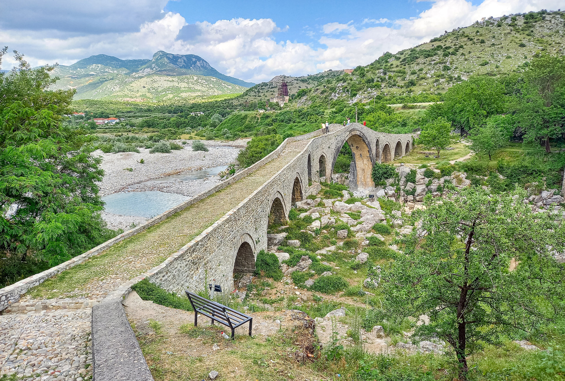 Eine gewölbte Steinbrücke mit mehreren Bögen führt über ein trockenes Flussbett zwischen Hügeln.