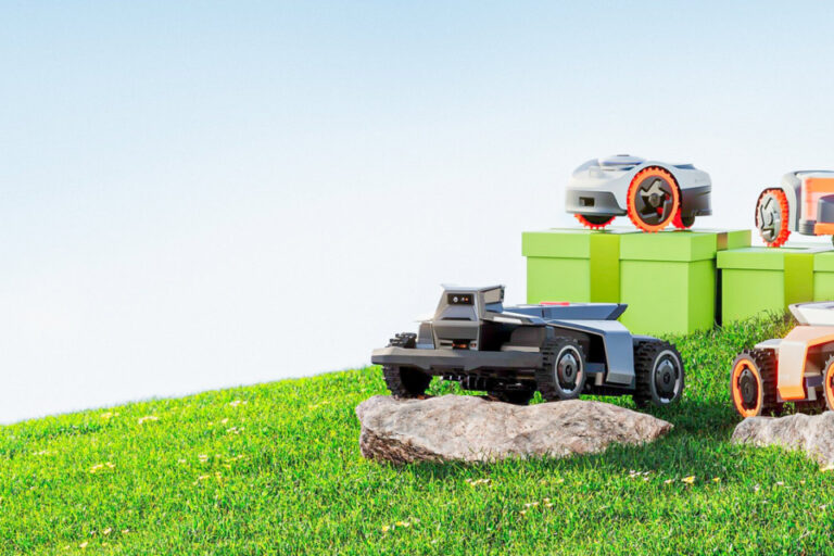 Zwei Mähroboter und weitere kleine Geräte stehen auf einer grünen Wiese neben Steinen.