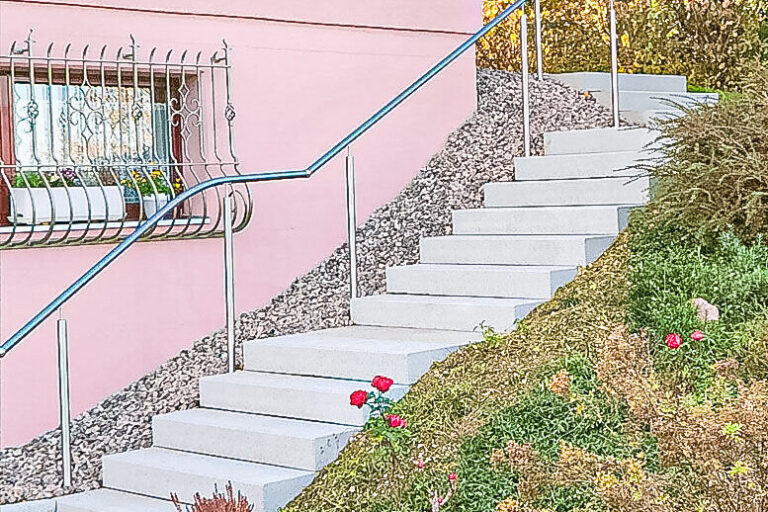 Eine Steintreppe mit geschwungenem Metallgeländer führt an einem rosafarbenen Haus vorbei einen Hang hinauf.