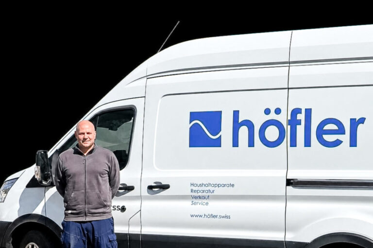 Ein Mann steht lächelnd vor einem weissen Lieferwagen mit dem Logo und Schriftzug „höfler“.