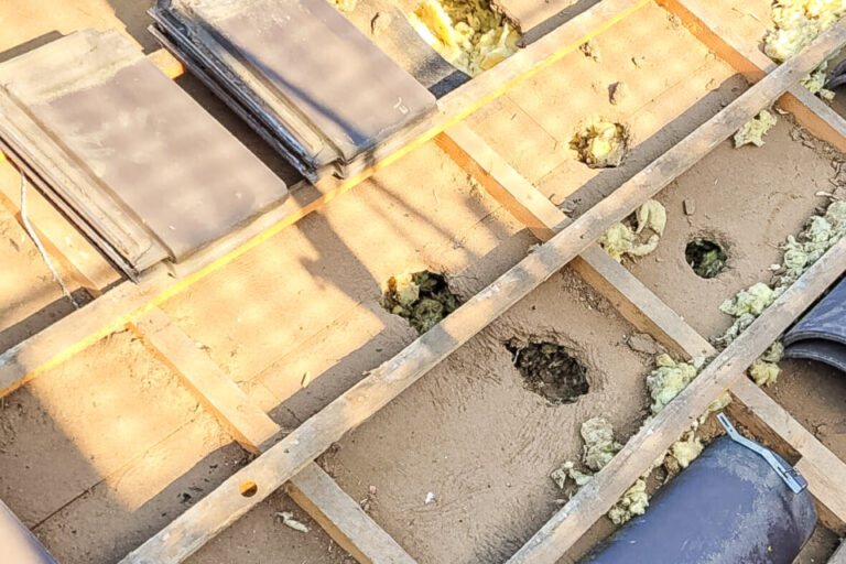 Blick auf ein Dach ohne Ziegel mit sichtbaren Holzlatten, Dämmmaterial und einzelnen losen Dachziegeln.