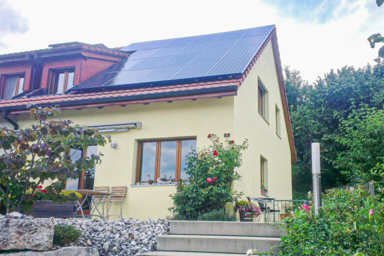 Gelbes Einfamilienhaus mit Solaranlage auf dem Dach und blühendem Garten davor.