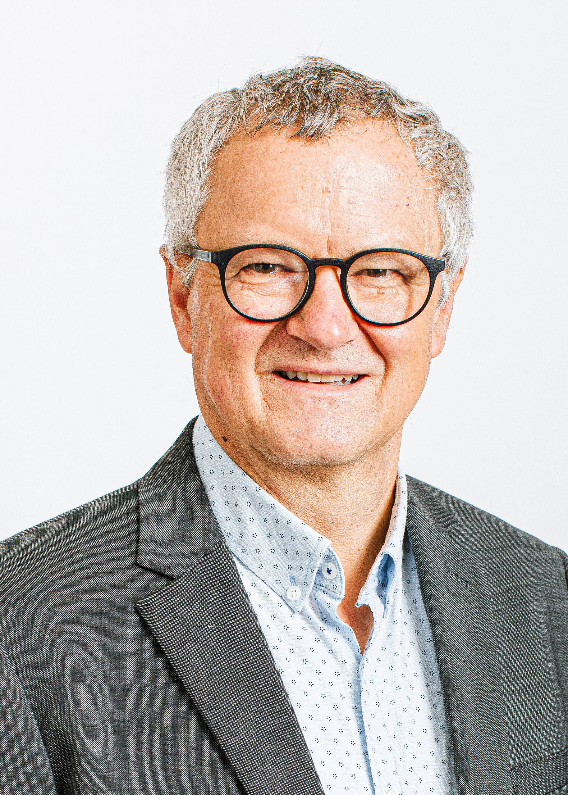 Ein älterer Mann mit grauen Haaren, Brille und Anzug lächelt in die Kamera.