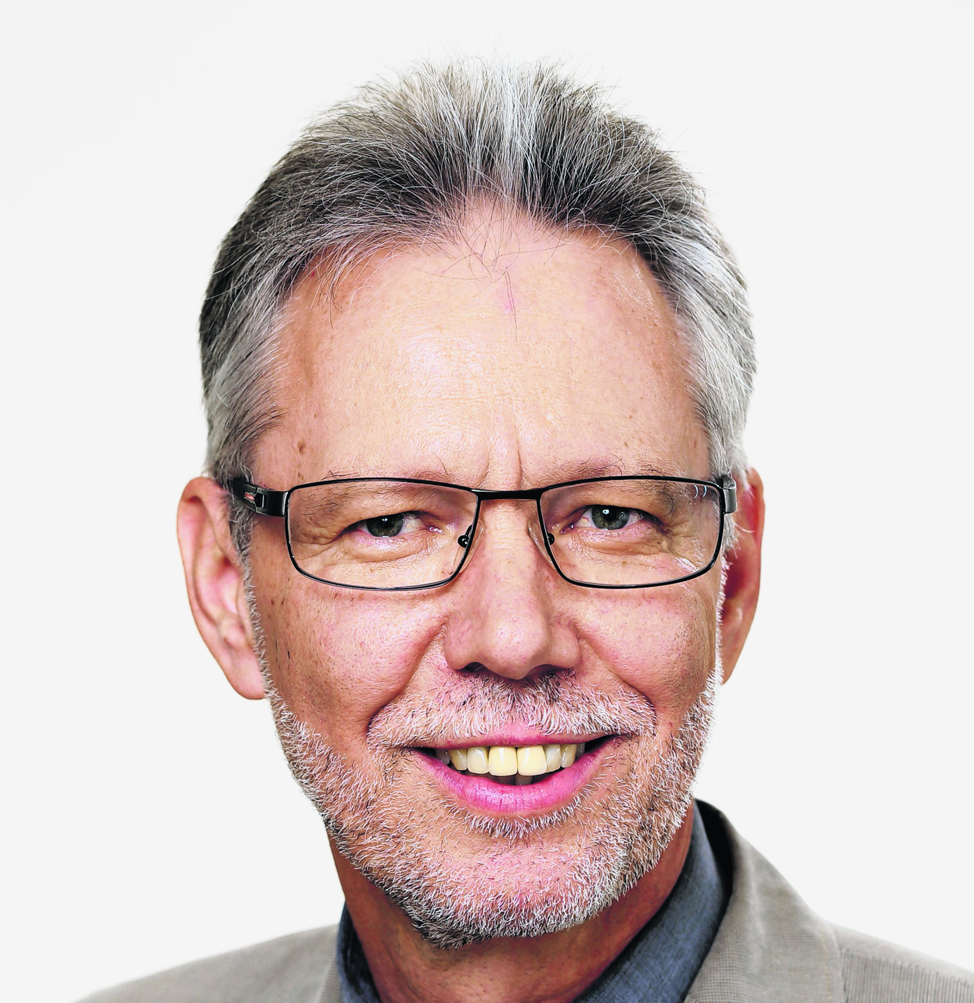 Ein älterer Mann mit grauem Haar, Brille und Bart trägt Anzug mit Krawatte und lächelt.