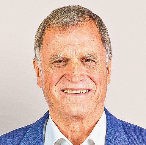 Ein älterer Mann mit grauen Haaren lächelt in die Kamera, er trägt ein blaues Jackett mit weissem Hemd.