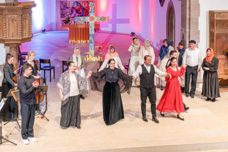 Sängerinnen und Sänger in historischen Kostümen sowie Musiker mit Geigen treten in einer Kirche auf.