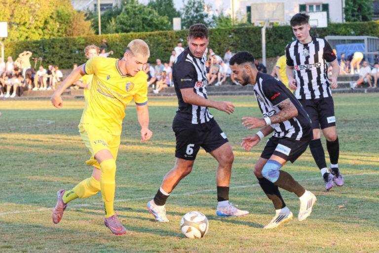 Spieler in Gelb und Schwarz-Weiß kämpfen auf einem Fußballfeld um den Ball.