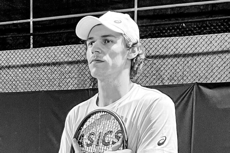 Ein junger Mann mit Kappe hält einen Tennisschläger an die Brust und blickt zur Seite.