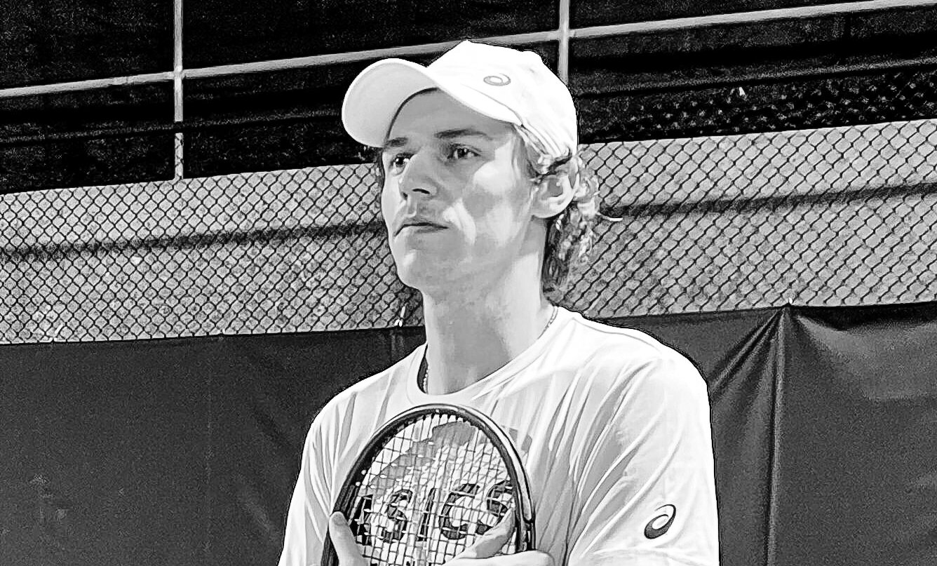 Ein junger Mann mit Kappe hält einen Tennisschläger an die Brust und blickt zur Seite.