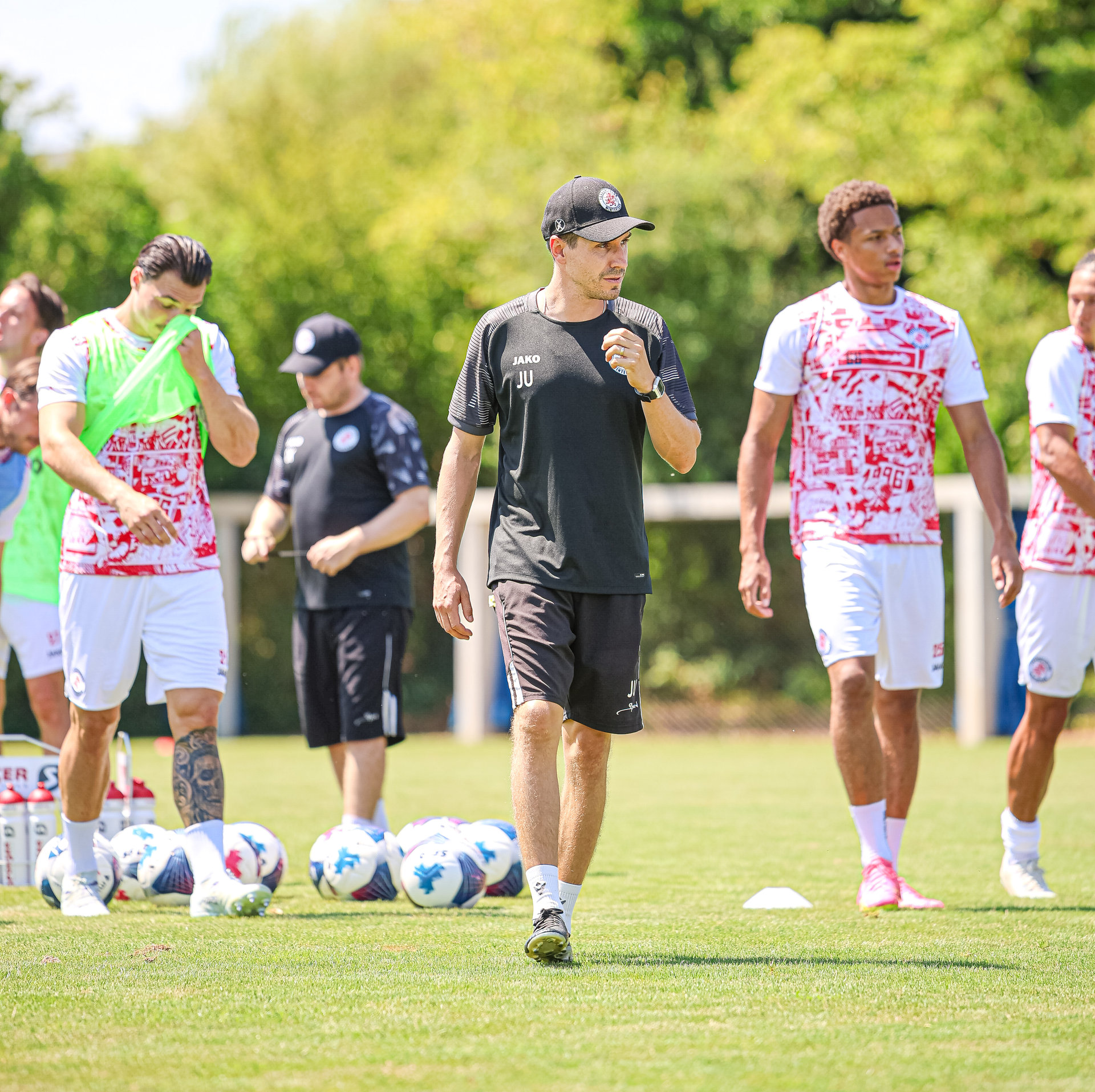 Fussballspieler und ein Trainer laufen bei einem Training über einen Rasenplatz.