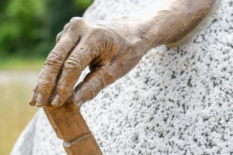 Eine bronzene Hand mit einem Meissel ragt aus einem grossen, runden Steinblock.
